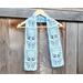 Display of the Flower Crochet Scarf on a hanger in front of a wooden fence.