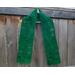 Dark green scarf with leaves along the length. It is on a hanger in front of a wooden fence.