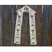 White scarf with snowmen along the length. It is on a hanger in front of a wooden fence.