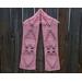 Pink scarf with hearts along the length. It is on a hanger in front of a wooden fence.