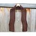 Display of the Zig Zag Crochet Scarf on a hanger in front of a wooden fence.