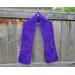 Purple scarf with hearts along the length. It is on a hanger in front of a wooden fence.
