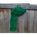 Another pic of the Leaf Crochet Scarf in green on a hanger in front of a wooden fence.