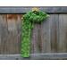 Variegated green scarf with trees along the length. It is on a hanger in front of a wooden fence.