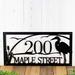 Close up of rectangular metal address sign with great blue heron, cattails, and and sunset lake scene, in matte black powder coat.