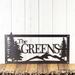 Rectangular personalized metal family name sign, with pine trees and mountain range, in silver vein powder coat.