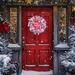 Rustic Christmas door wreath with red and white ribbons on a red door, ideal for farmhouse holiday front door decor.