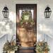 Rustic fall tobacco basket wreath on a wooden front door with berries, greenery, and a 'Fall Is In The Air' sign. Autumn porch decor.