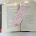 The romantic bookmark is sitting in the middle of an open book with fairy lights around the book on a white table