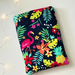 This tropical book sleeve has navy background with flamingos, tropical leaves and flowers in bright colors