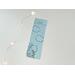 this blue bookmark has a blue background with a girl reading in the bottom left hand corner with clouds in the sky