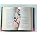 this ornament book mark is in the middle of an open book with fairy lights above the book