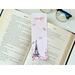 Eiffel Tower book mark is on top of an open book with a pair of glasses above the book on a white table