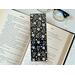 this elegant bookmark is in a real life setting with an open book and a pair of glasses on a white table