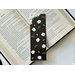 this floral bookmark has a black background with white flowers and green leaves and hearts all over the page holder.