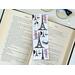 the Paris book mark is on top of an open book with a pair of glasses on a white table