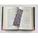 the laminated bookmark is in the middle of an open book with fairy lights around the book on a white table