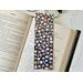 the flower bookmark is on top of an open book with a pair of glasses above the book and fairy lights on the right side of the book on a white table