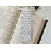 the laminated bookmark is on top of an open book with a pair of glasses above the book and fairy lights on the right side on a white table