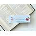 the laminated bookmark is on top of an open book on a white table