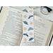 this bug book mark is on top of a open book with a pair of glasses in the back on a white table