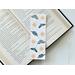 This moth bookmark has a white background with moths being beige and green. There are stars and moons all over the page saver