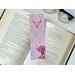 this cowgirl bookmark is on top of an open book with a pair of glasses on a white table