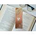 the laminated bookmark is on top of an open book with a pair of glasses and fairy lights on the left side on a white table