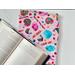 The candy book sleeve on a white table with fairy lights on the left side and an open book a little on top of the book jacket