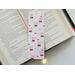 this cherry bookmark has a light pin background with cherries having pink bows on the them, and the smaller ones not having bows on them.