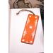 Front of bookmark with orange background, hand painted paw prints and various dot art designs in white. Jute rope tassel.