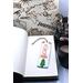 Front of bookmark, white background, red lettering, Christmas Tree and jute rope tassel.