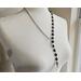 Asymmetrical lariat necklace: one side black coin beads, silver spacers, pewter dangle, other side rhodium chain connected by pewter loop