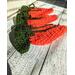 Angled side view of medium orange crochet carrots with dark green tops to show unfilled thickness which is around 1/4 inch.