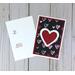 A valentine card making kit of 12 with black scrapbook paper with hearts, white and red heart embellishments, and white cards and envelopes.