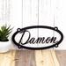 Personalized oval metal sign with child name, in matte black powder coat.