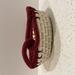 A small round woven cream basket with a wine colored decorative knot design on the rim.