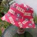 Side view of bucket hat on stand. Fabric has red and gold SF 49ers logos on red background.