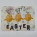 Yellow chicks wearing bunny ears and shiny pink cheeks accented with paint with Easter spelled out in chocolate 