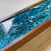 A close up of the design of this mango wood tea box with a hinged top.  The design features swirls of blue, teal, periwinkle and white.