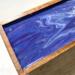 A close up of the top of this mango wood tea box shows ribbons of various shades of rich purple and white forming a pleasing design.  The glossy finish makes the colors even richer and adds interest and luxury to your home decor.