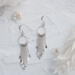  Pair of 925 sterling silver fringe dangle earrings displayed on a textured white surface with flowers and crystals.
