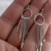  Close-up of a hand holding a pair of 925 sterling silver fringe dangle earrings with multiple dangling elements.  
