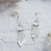  Pair of 925 sterling silver fringe dangle earrings displayed on a textured white surface with flowers and crystals.
