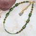 An 18-inch handmade necklace with vintage olive-green glass beads, bicones, and seed beads on a gold-plated stainless steel chain
