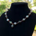 Moss agate beads in shades of teal, green and blue are linked by wire wrapping to form a necklace with copper clasp. 