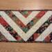 Small table runner with elegant red, green, and black fabric in a chevron pattern.