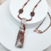 Handmade necklace with jasper pendant, garnet beads, and copper chain on a marble background.