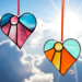 Heart-sun stained glass ornaments hanging in front of a blue sky with white puffy clouds, background.