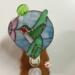 Hummingbird stained glass night light- made of green white and red glass, background is of light blue glass with a pink flower and lampworked green leaf. Show with light off.